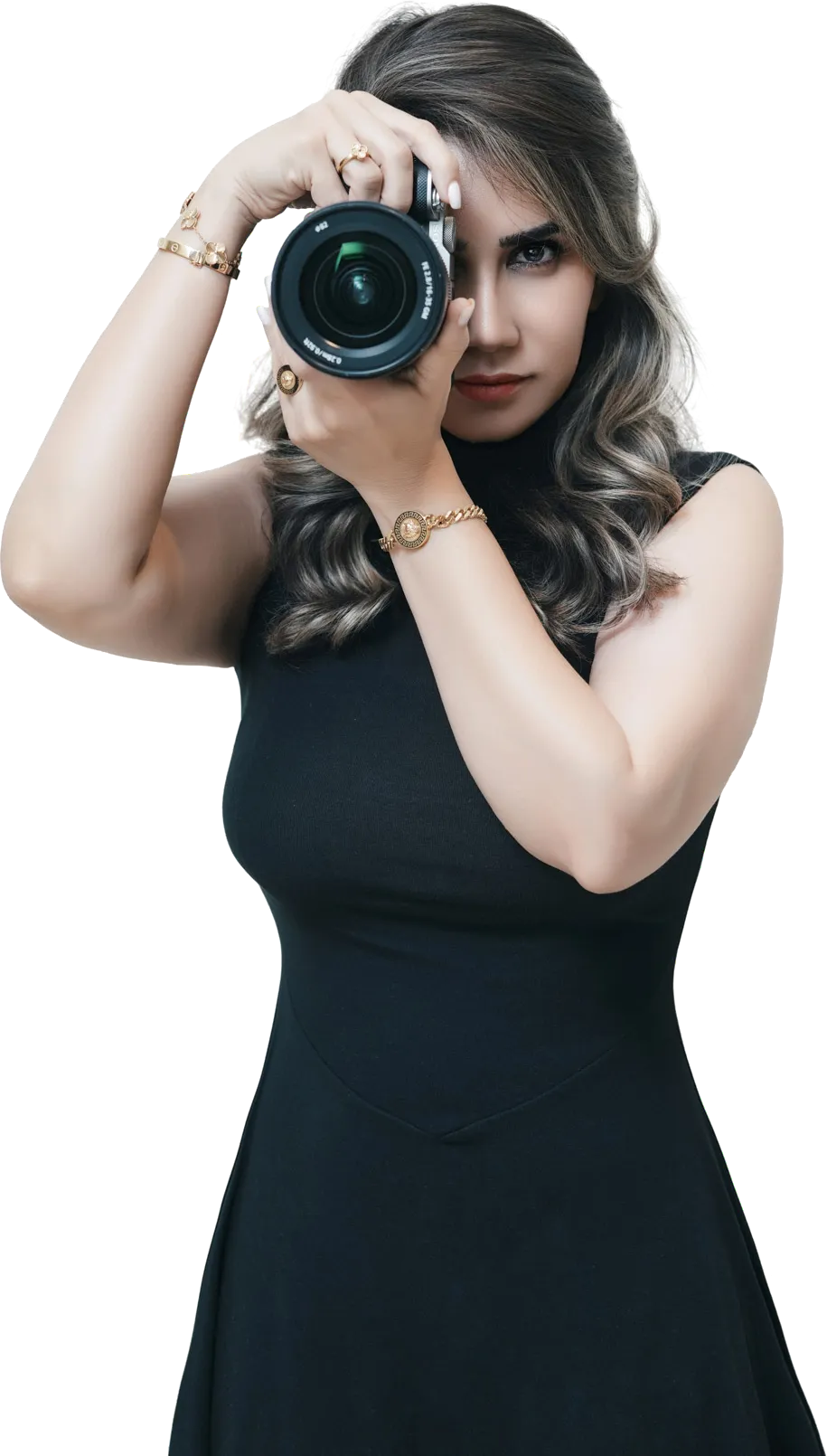 Atrin in a black dress raising a camera to her eye, gold bracelets on both wrists