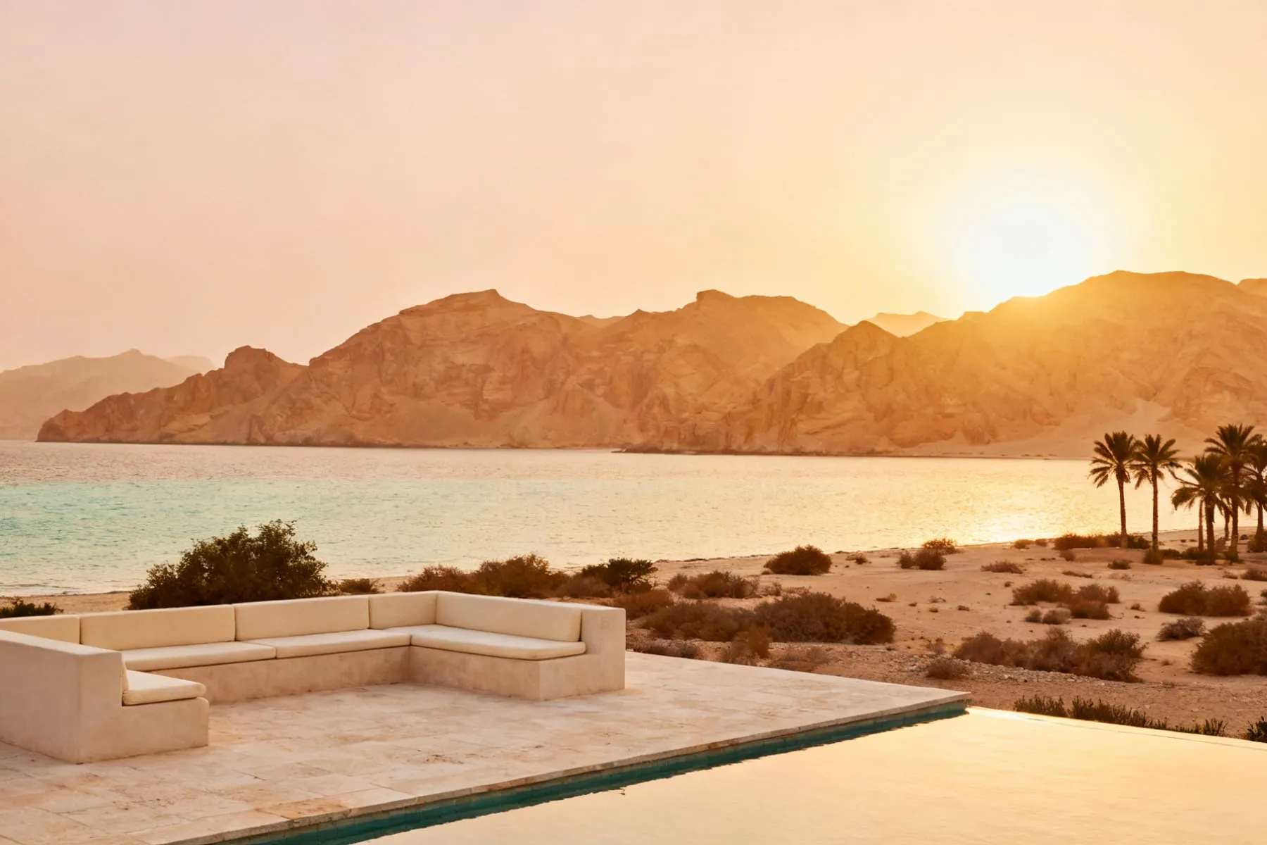 A resort terrace above a quiet shore, ochre mountains beyond at sunset