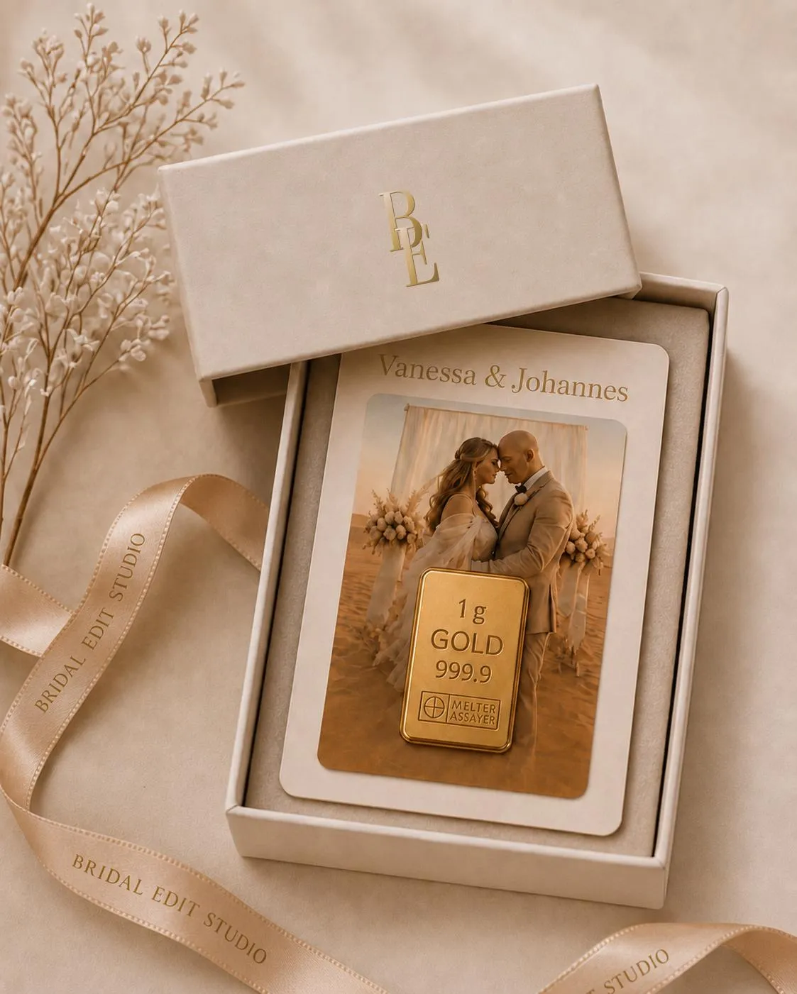 An open Bridal Edit Studio keepsake box, its lid embossed with the BE monogram — inside, a personalised card carrying the couple's names and photograph, set with a 1g 999.9 fine-gold bar, beside a branded champagne ribbon