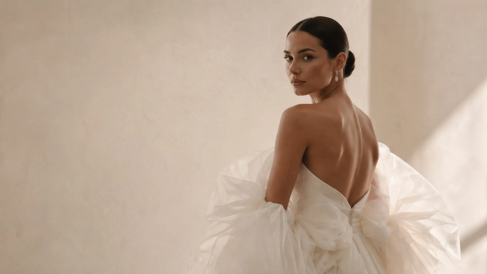 A bride in a tulle gown turning to camera against a sunlit plaster wall