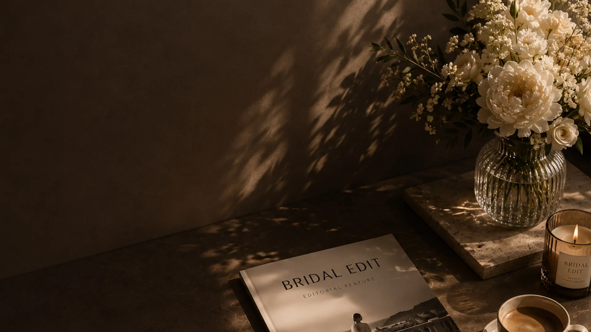 A Bridal Edit editorial feature on a dark stone surface in low evening light, white blossom and a lit candle beside it